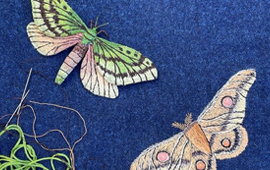 Pink and green embroidered butterflies are stitched into a blue background