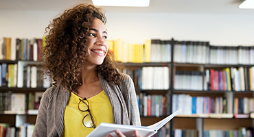 Woman holding an open book in front of library shelves