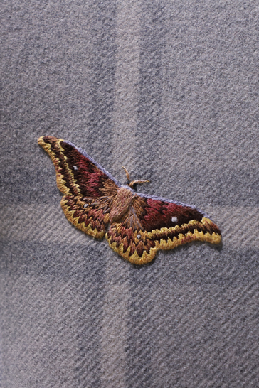 An embroidered yellow and maroon moth is stitched onto a grey plaid armchair