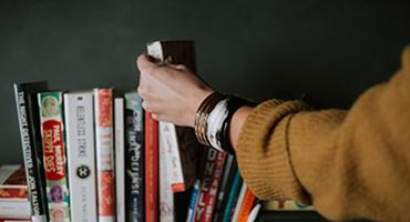 Hand selecting a book from a shelf of books