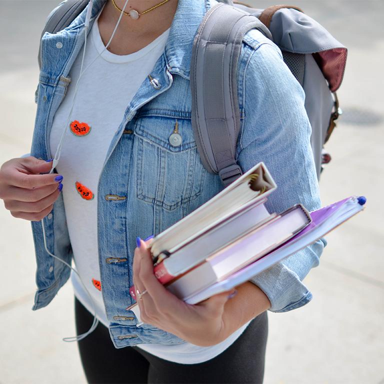 Woman with backpack, holding stack of books in one arm