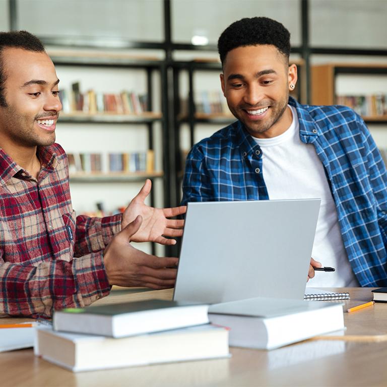 Two men sitting at laptop, smiling at screen