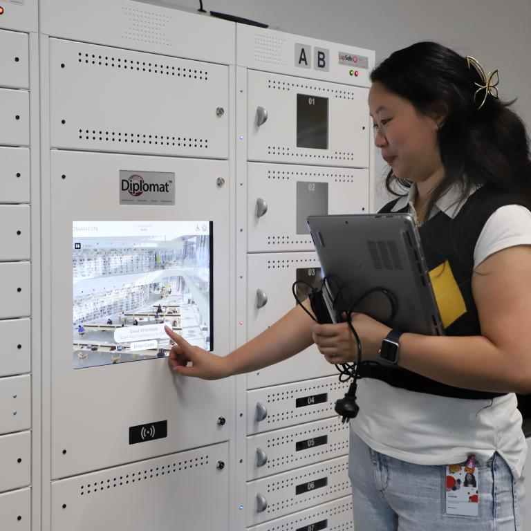 Student holding a laptop pressing the touchscreen of a locker to return her loan