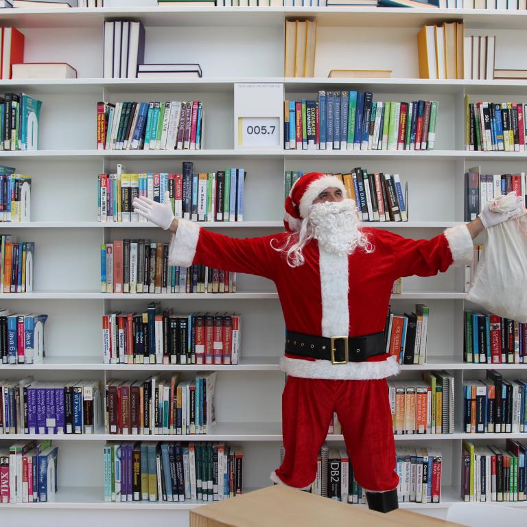 Santa standing in front of a book shelf with his present bag