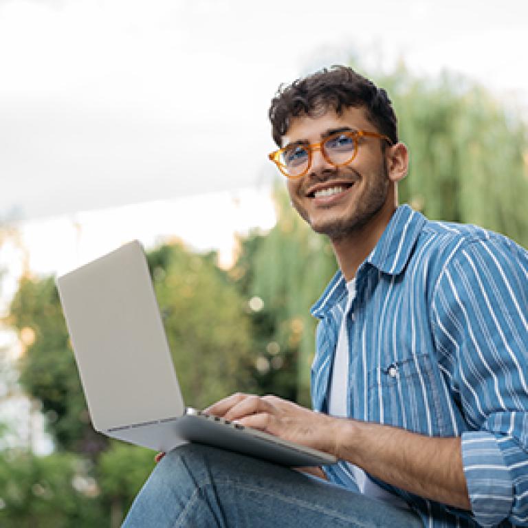 Man wearing glasses sitting with laptop on his knee and smiling